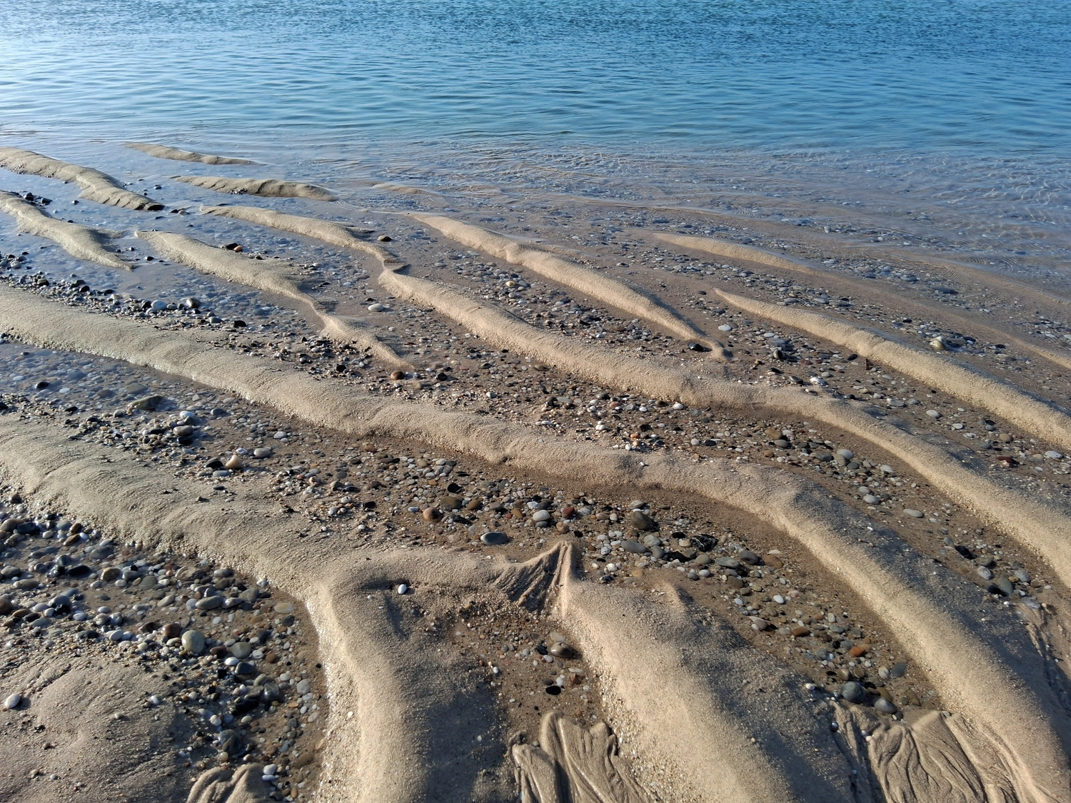 Hebamme Trauma-Fachberaterin - Coaching, Beratung, Kurse und Lesungen - Eine natürliche Küstenlandschaft, in der Wasser über ein Bett aus Sand und Kieselsteinen fließt.