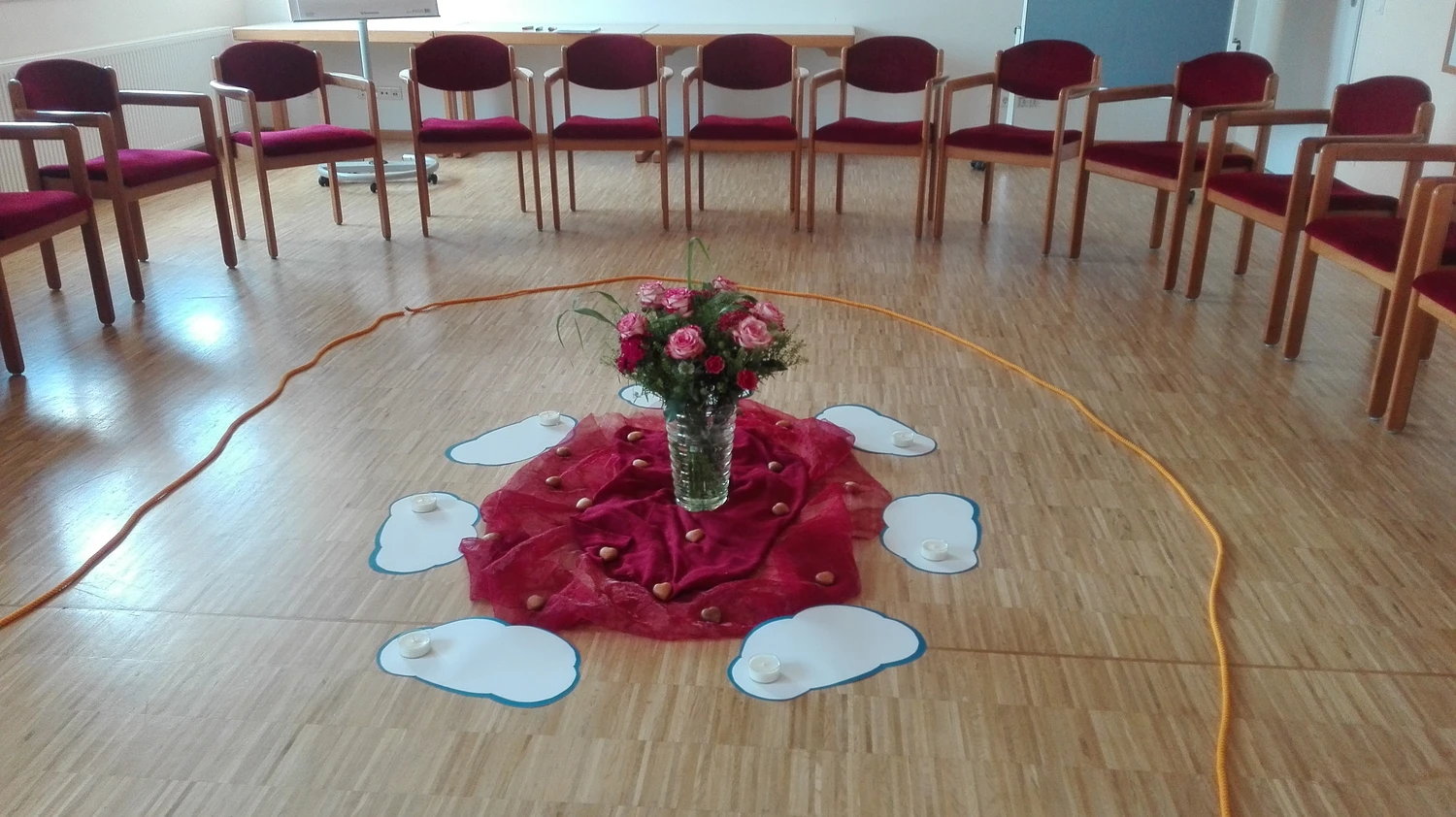 Hebamme Trauma-Fachberaterin - Coaching, Beratung, Kurse und Lesungen - Eine kreisförmige Anordnung von Stühlen um einen zentralen Bodenbereich mit Blumen und dekorativen Stoffen.